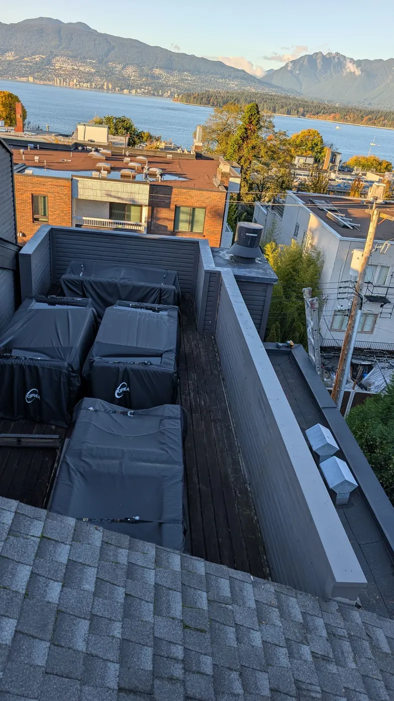 Painted rooftop deck parapet caps and dark siding overlooking English Bay and the North Shore mountains in Vancouver