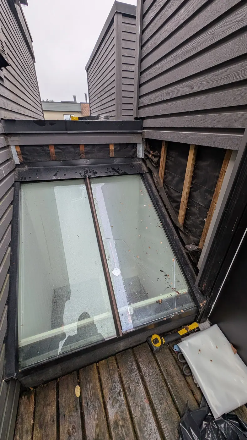 Exterior wall opened to exposed sheathing and house wrap beside a skylight, showing the wood framing during a carpentry repair project in Vancouver, BC.