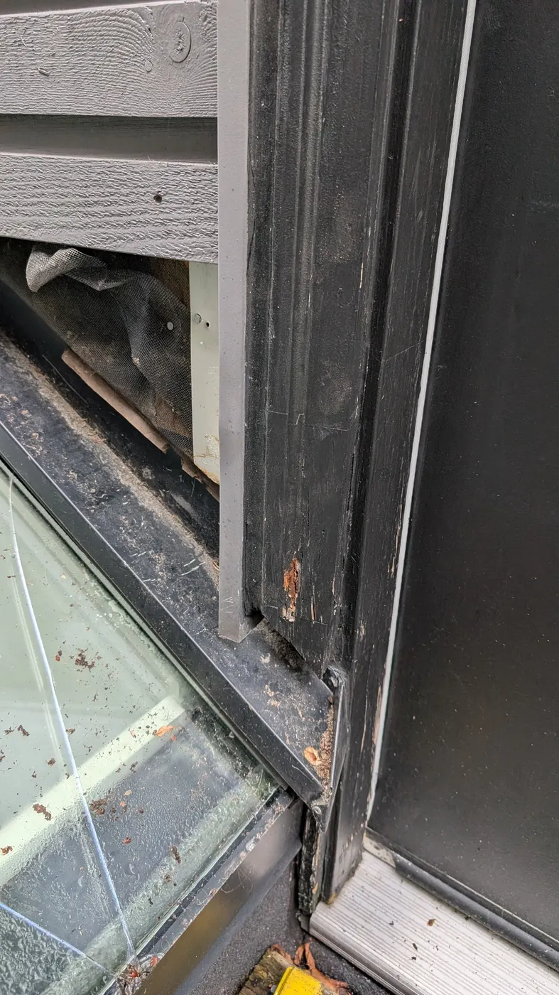 Close-up of rotted wood window trim and weathered black frame corner on a Vancouver, BC home, showing decay in need of carpentry repair.