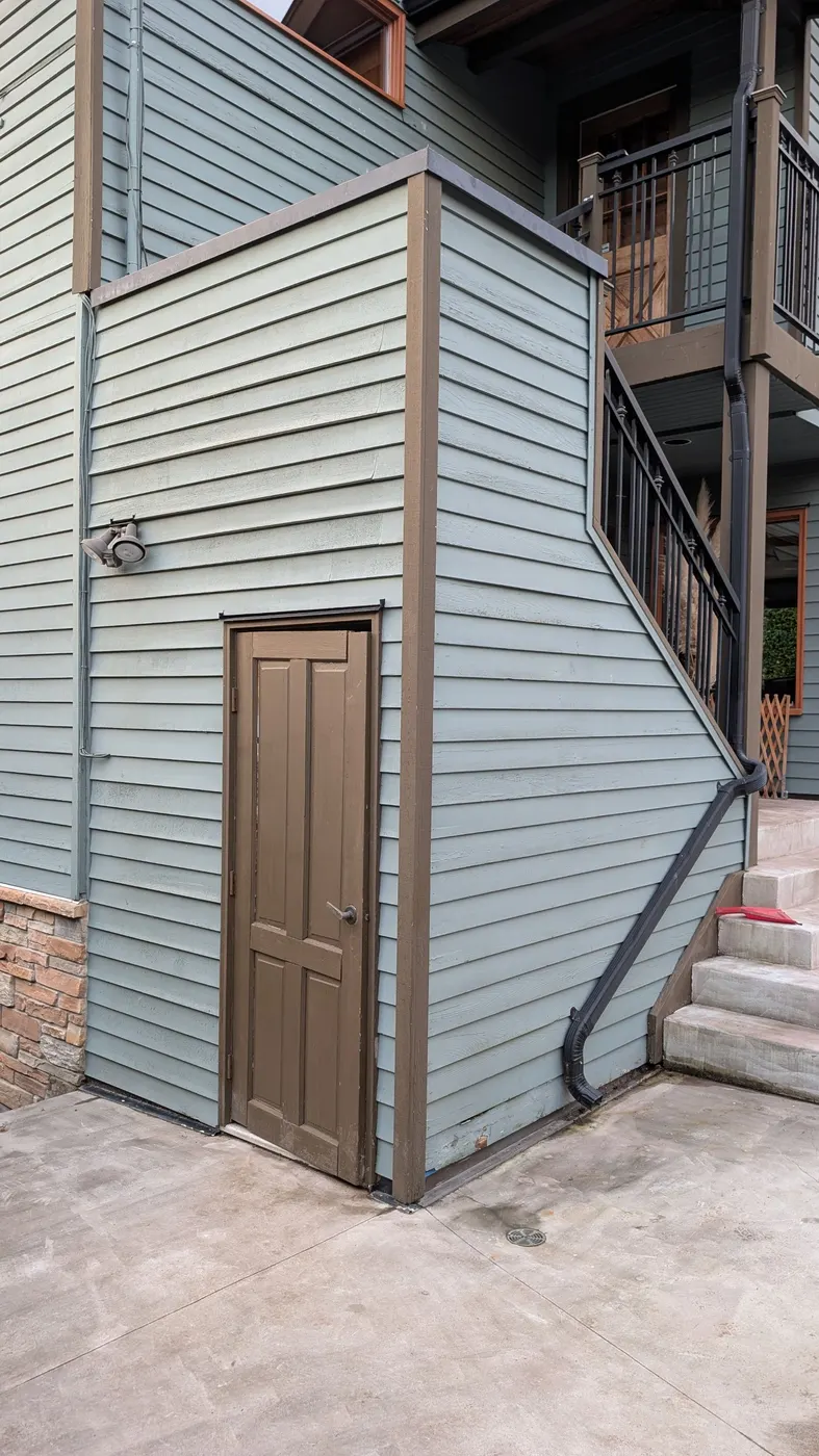 Rebuilt exterior corner of a home addition with a new brown door and blue-gray siding in Vancouver, BC.