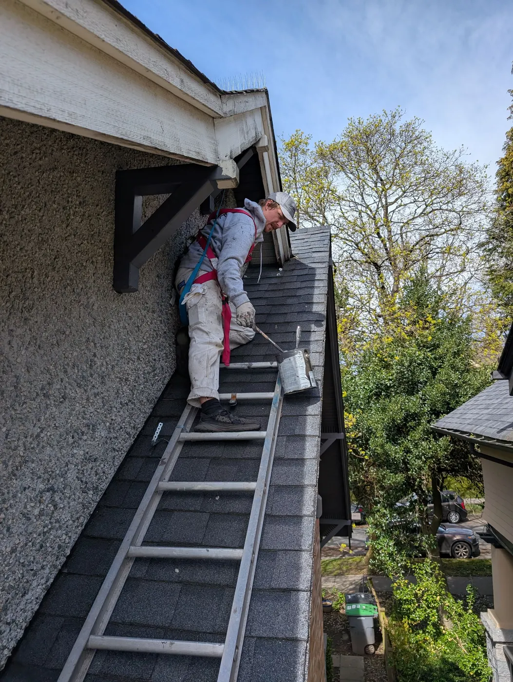 Painter on a ladder cutting in dark trim paint along a gable roofline in Vancouver, BC.