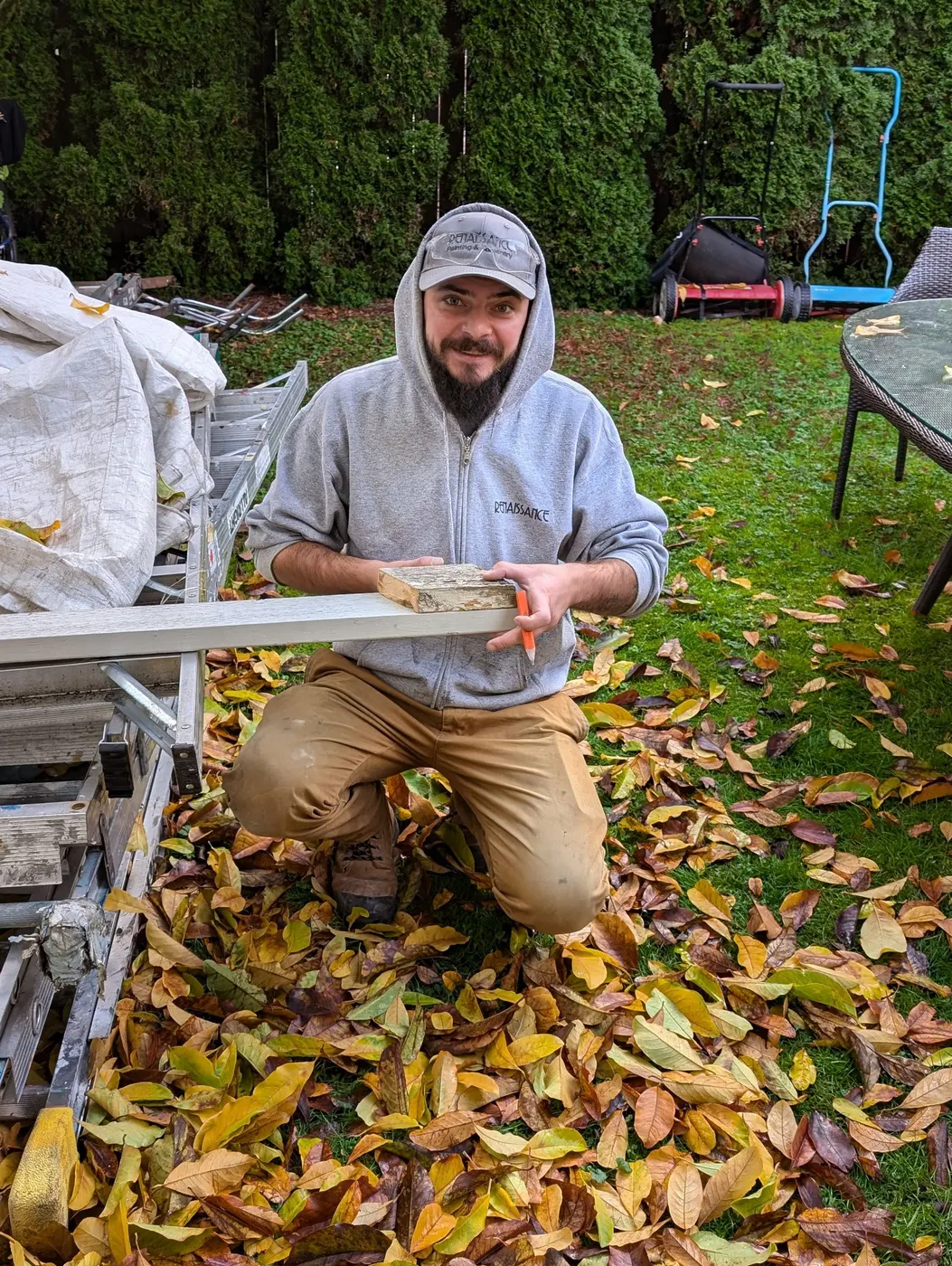 Renaissance Painting carpenter holding a length of replacement trim beside ladders and materials during an exterior project in Vancouver, BC.