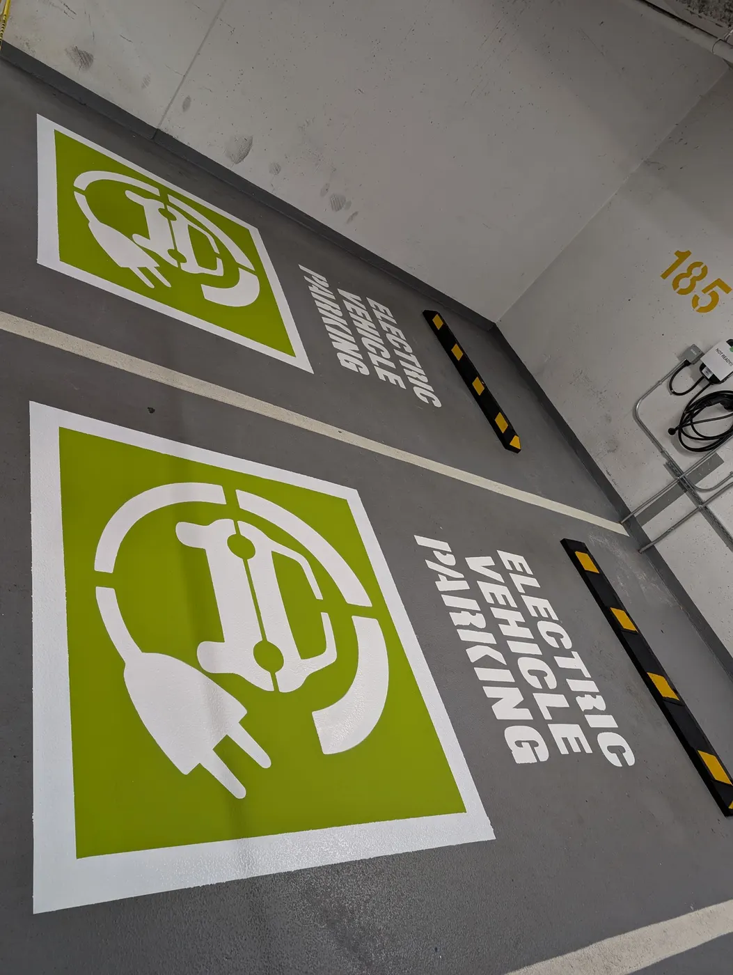 Close-up of two finished green Electric Vehicle Parking floor stencils in a Vancouver parking garage.