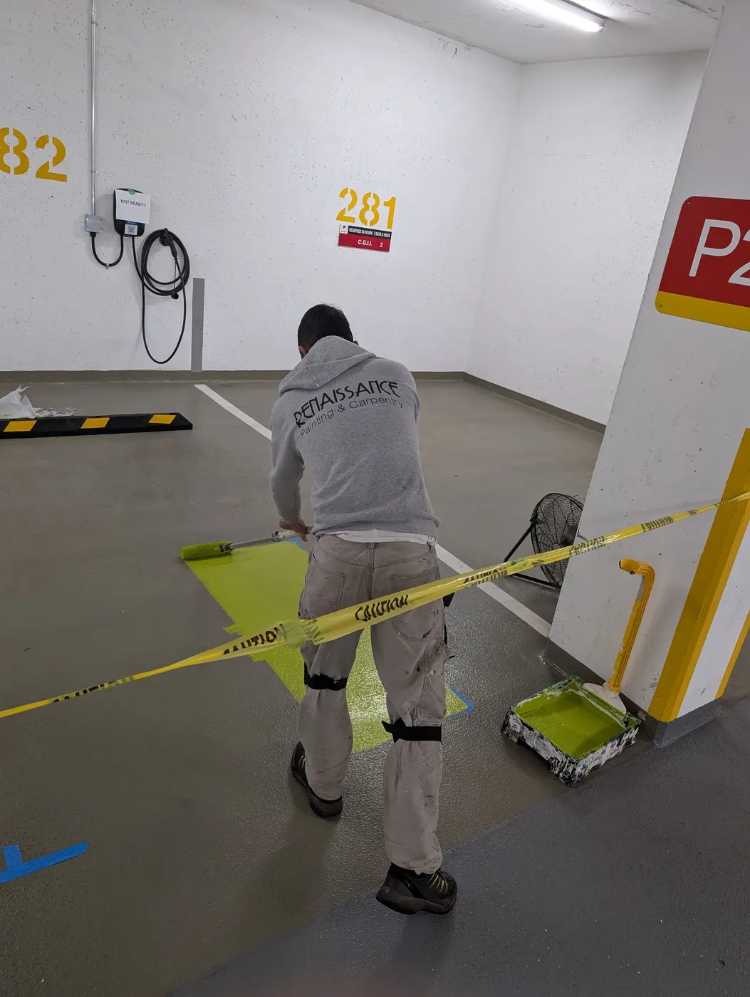Renaissance Painting and Carpentry crew member in branded workwear rolling green epoxy coating onto a Vancouver parkade floor.
