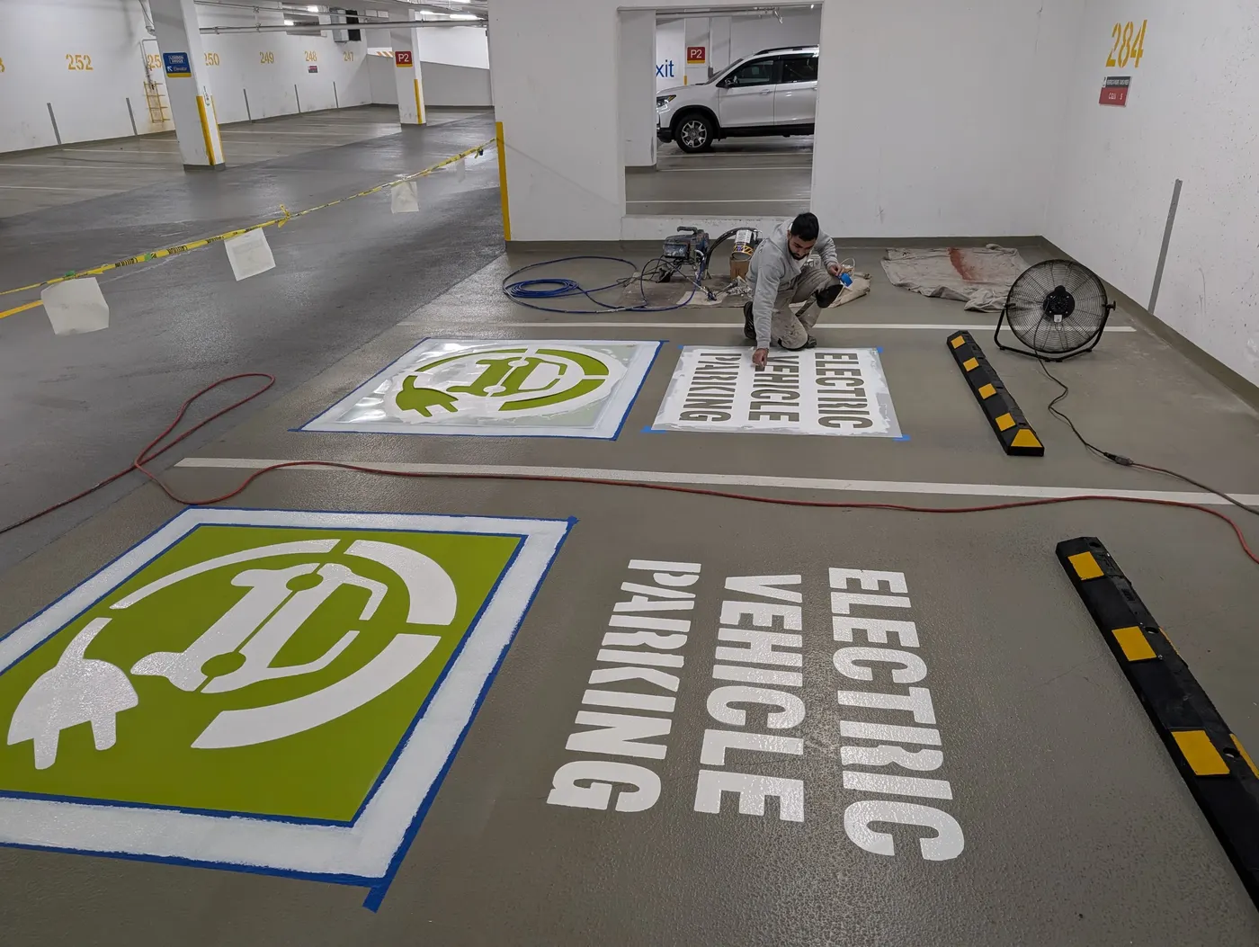 Wide view of a Vancouver underground parkade corridor showing multiple EV parking stalls being painted and stenciled.