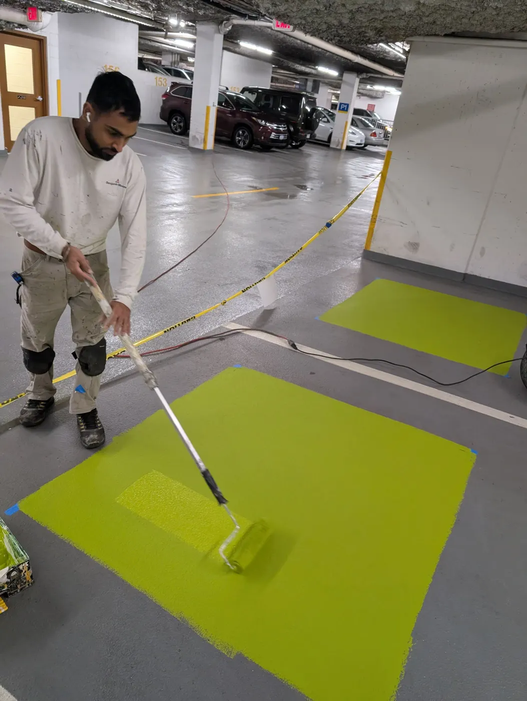 Painter rolling green epoxy floor coating in a busy underground parking garage in Vancouver, BC.