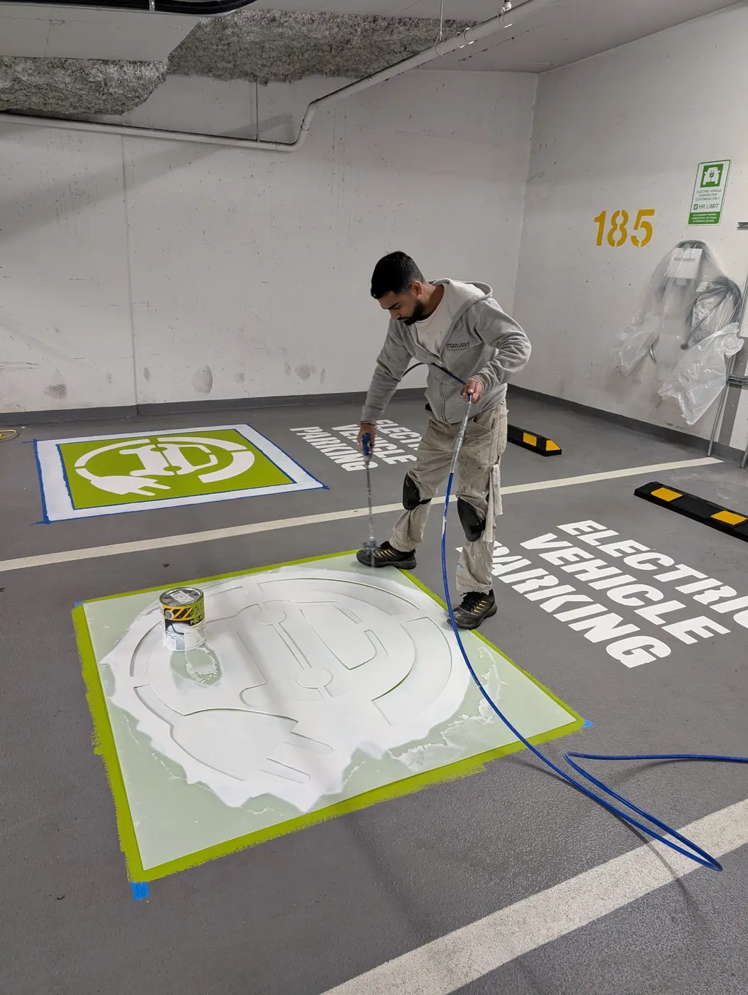 Renaissance Painting crew member spray-applying green epoxy floor coating for an EV parking stall in Vancouver.