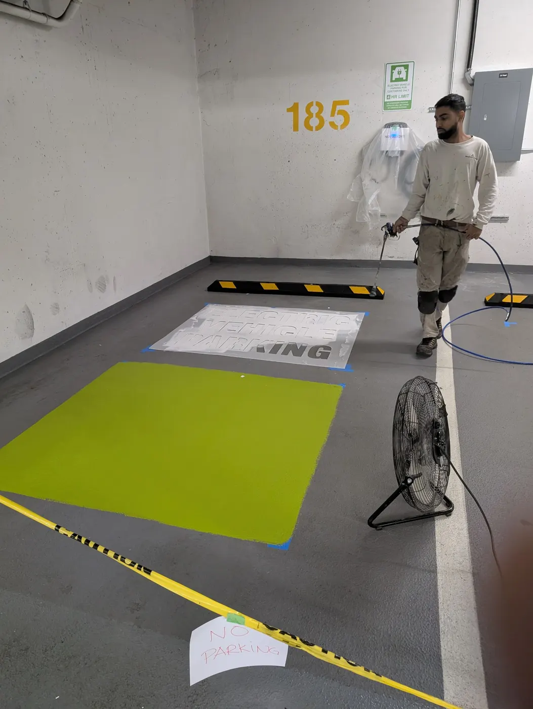 Painter stenciling an Electric Vehicle Parking floor graphic in a Vancouver condo parking garage.
