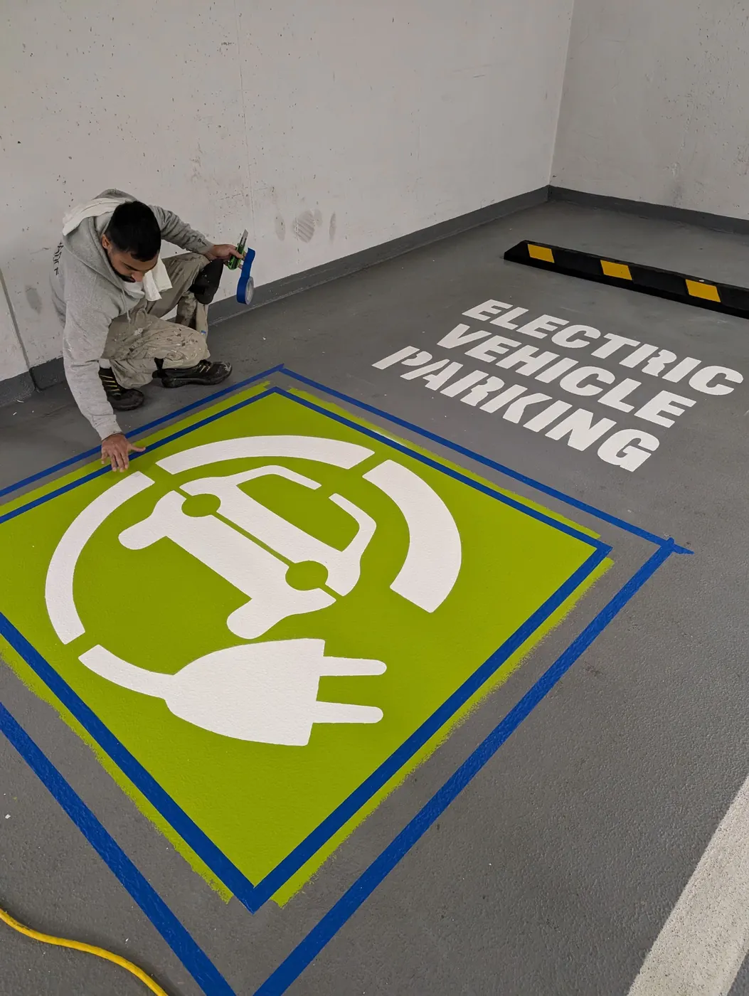 Painter taping down an electric vehicle charging symbol stencil before painting a Vancouver parkade floor.