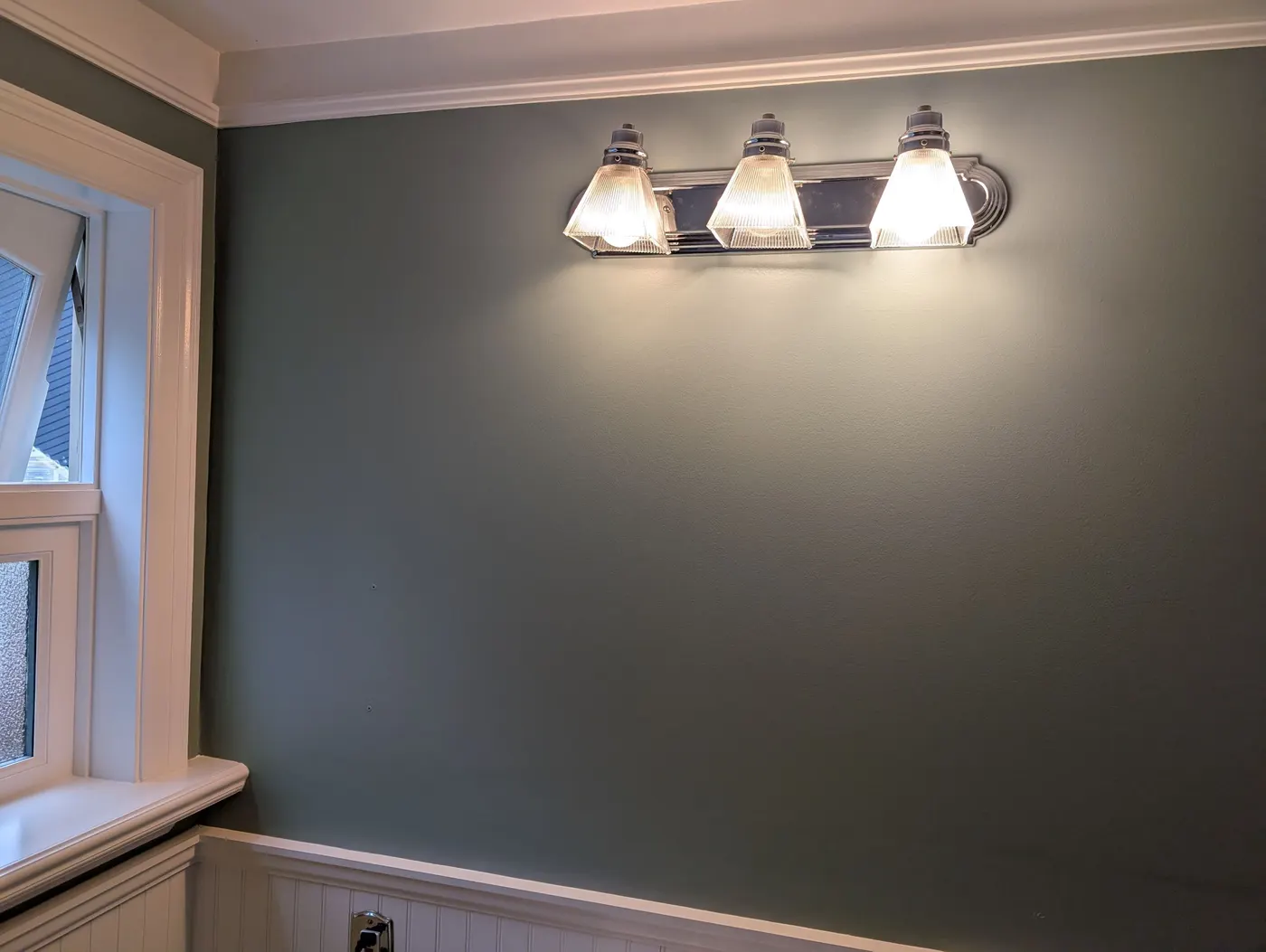 Freshly painted sage green bathroom vanity wall with vintage-style triple light fixture in a Vancouver, BC home renovation by Renaissance Painting.