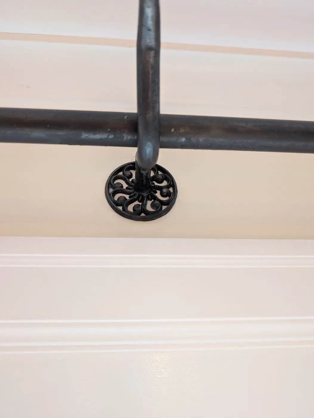 Decorative black curtain rod bracket mounted against a freshly painted cream ceiling and wainscoting in a Vancouver, BC interior.