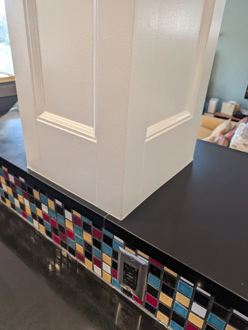 Finished white paneled kitchen island column with colorful mosaic tile base in a Vancouver, BC dining and kitchen area.
