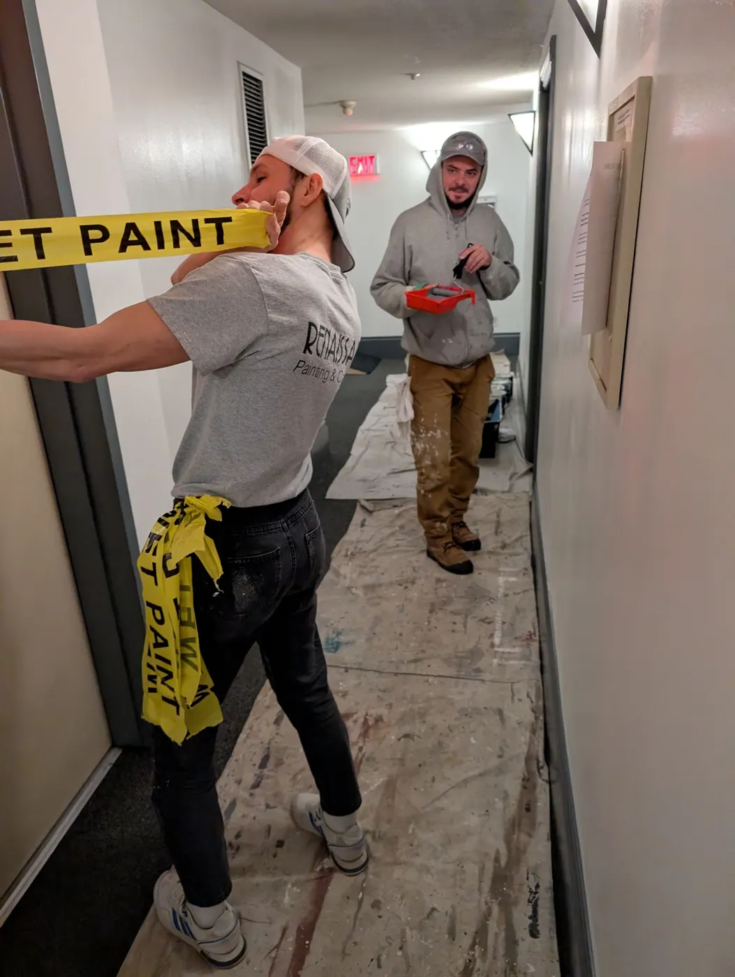 Two Renaissance Painting crew members in branded grey t-shirts standing behind wet paint tape in a Vancouver condo hallway during a repaint.
