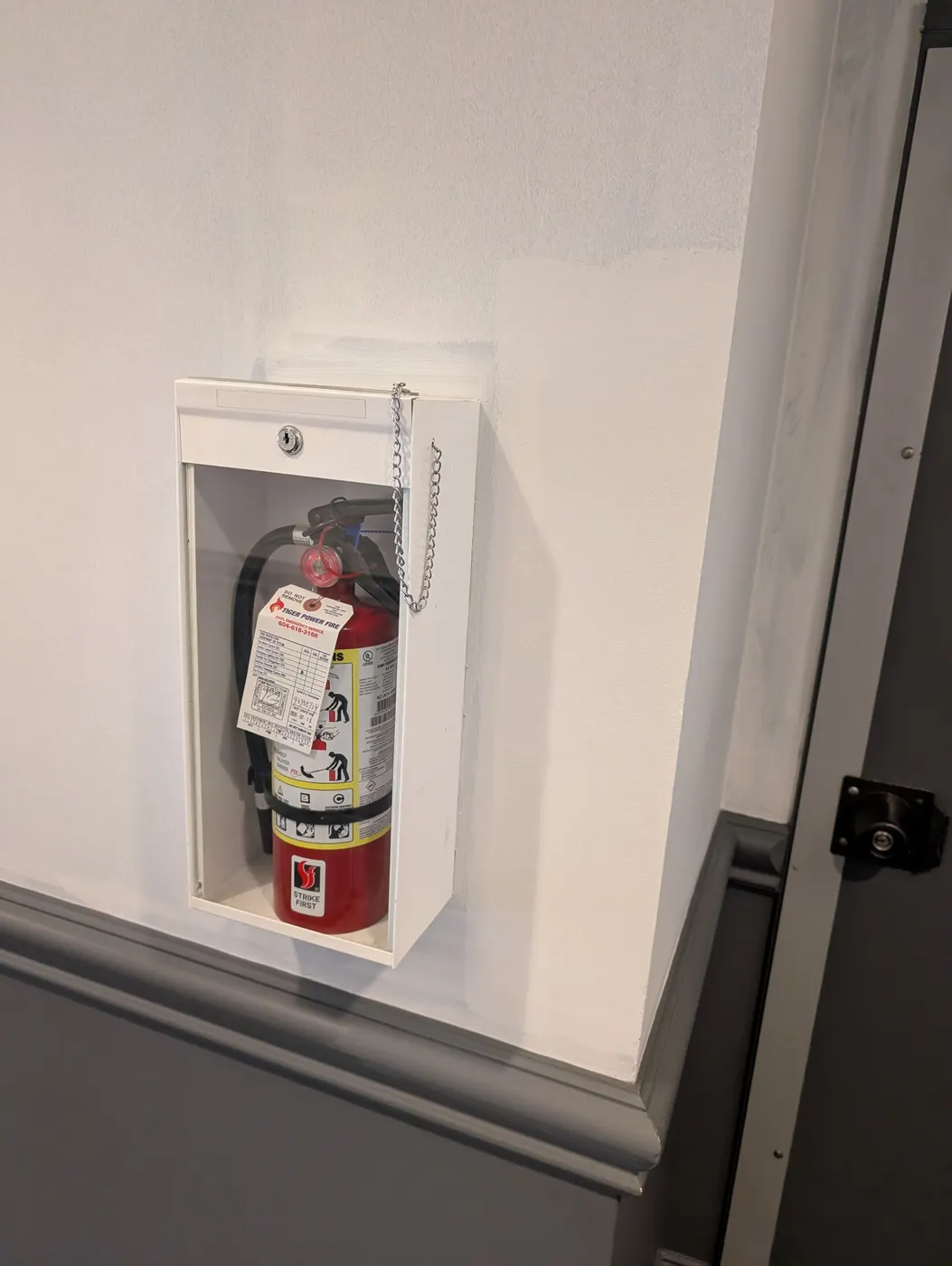 Precise paint cut-in around a wall-mounted fire extinguisher cabinet during an interior repaint in a Vancouver building.