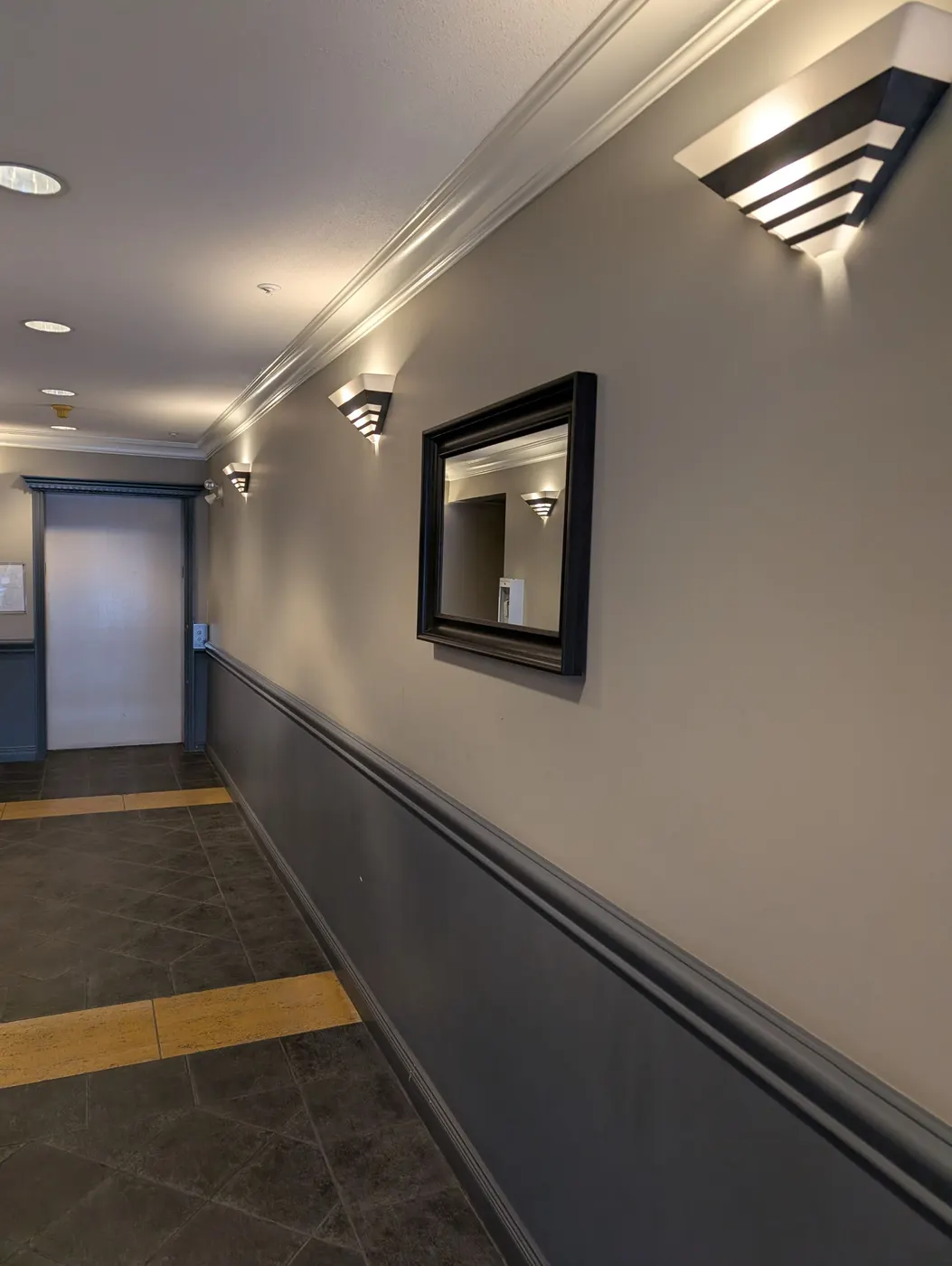 Angled view of a repainted Vancouver apartment hallway showing clean paint lines along crown moulding, wall sconces, and a framed mirror.