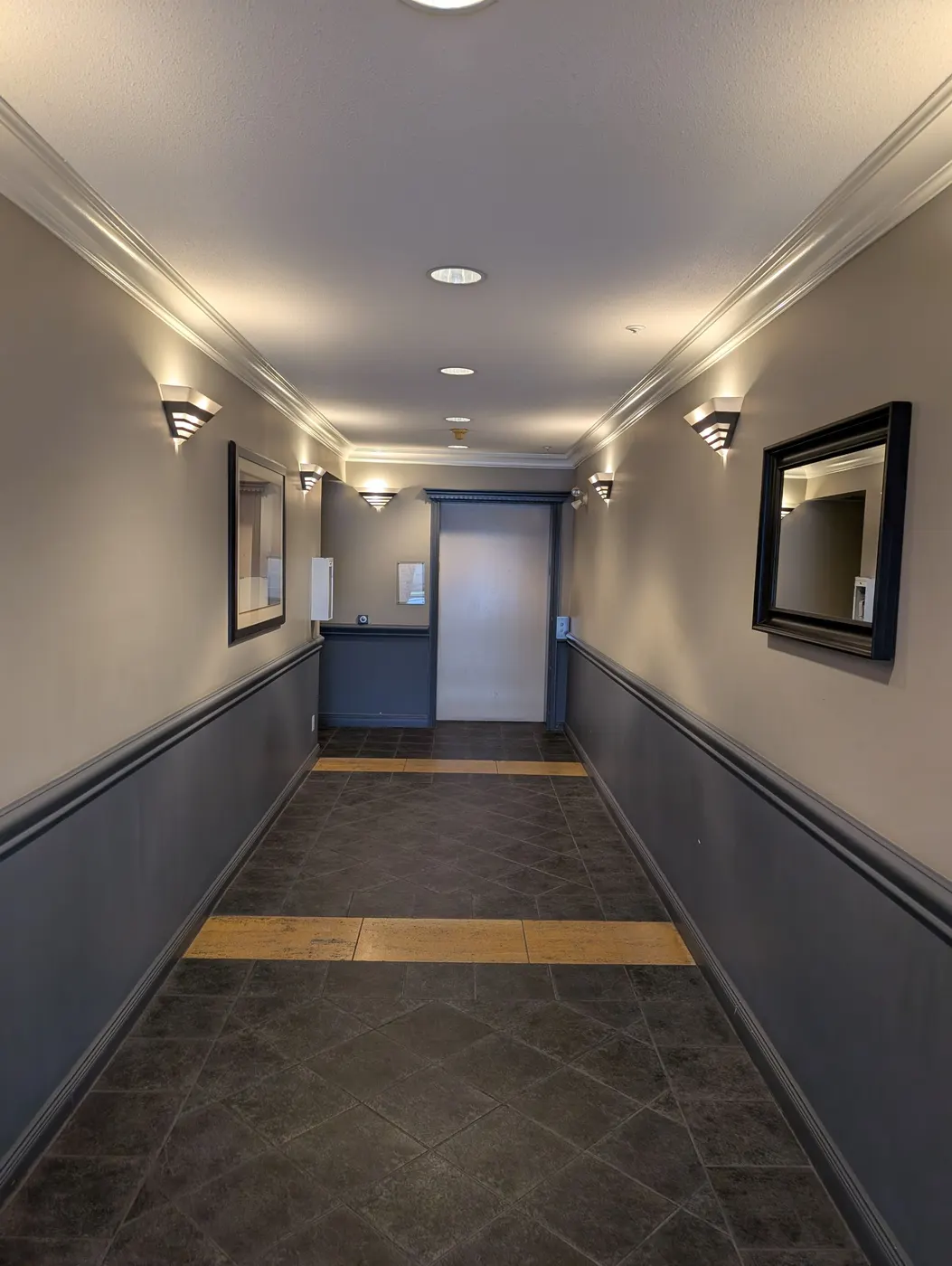Freshly painted condo hallway in Vancouver, BC with charcoal grey wainscoting and warm taupe upper walls, crown moulding, and wall sconce lighting.