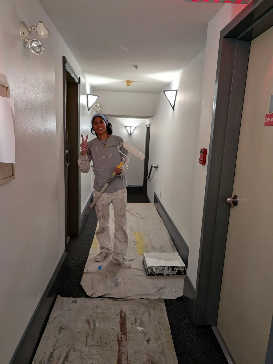 Renaissance Painting team member rolling fresh white paint onto a Vancouver condo hallway wall, smiling with a paint roller in hand.