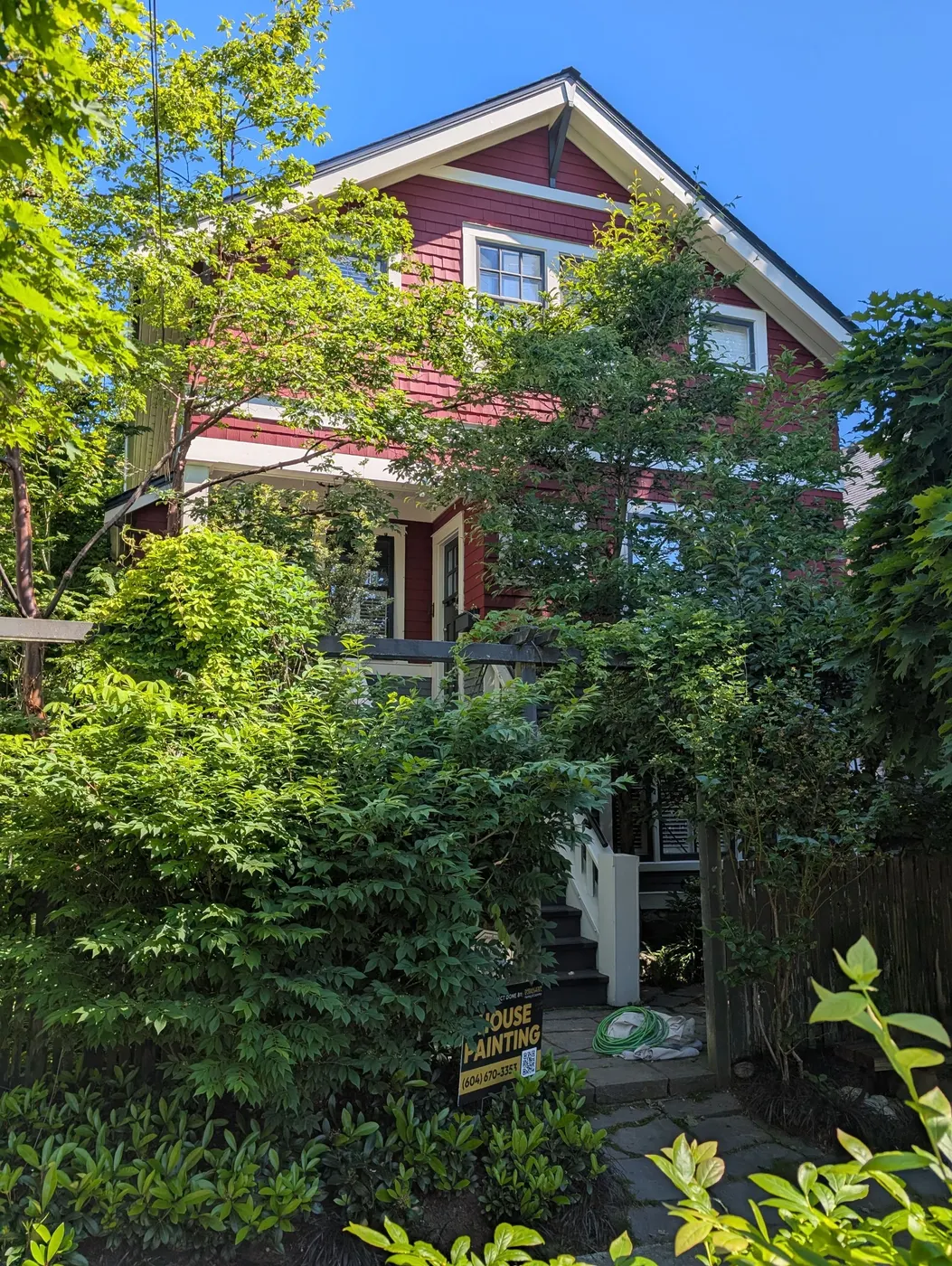 Completed exterior paint job on a red craftsman home in Vancouver, BC with a Renaissance Painting yard sign, photographed on a sunny day at project wrap-up.