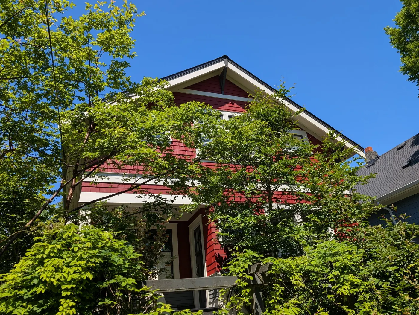 Freshly repainted red craftsman home exterior in Vancouver, BC with crisp white trim, photographed under blue sky after the project's completion.