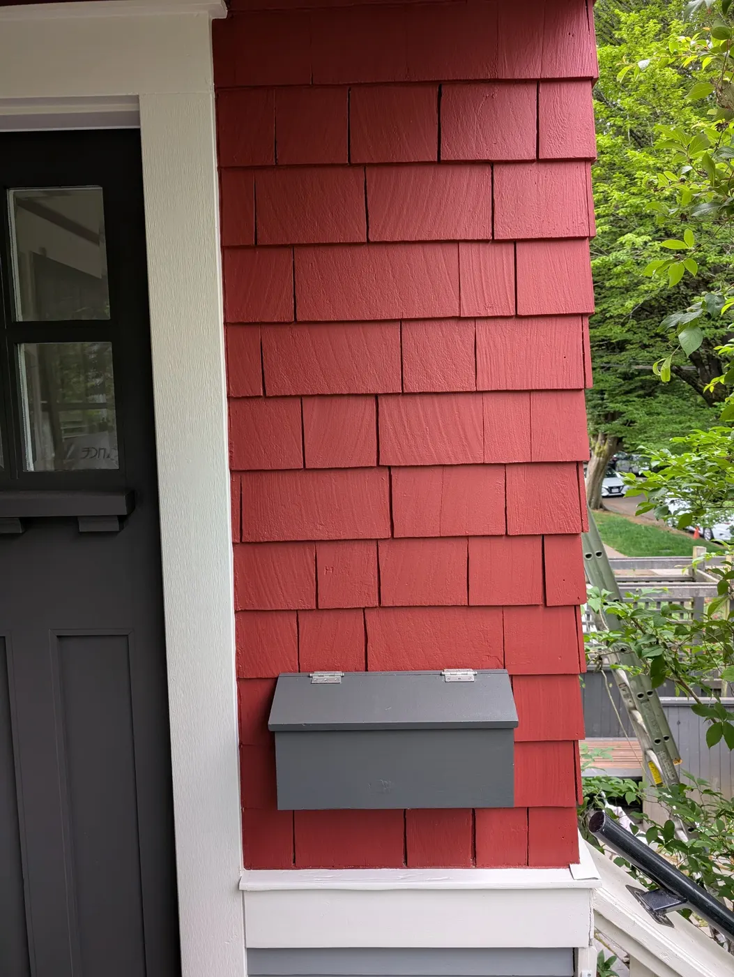 Close-up of freshly painted red cedar shingle siding and a charcoal front door on a Vancouver, BC home after an exterior repaint.