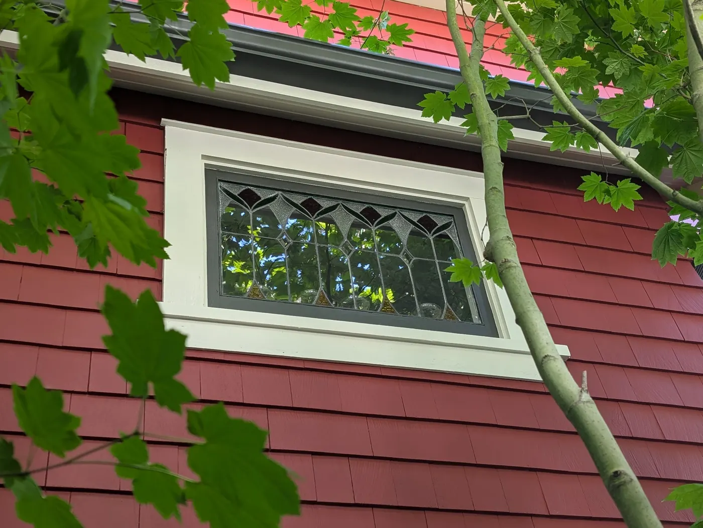 Freshly painted red siding around a leaded glass window on a Vancouver, BC craftsman home after Renaissance Painting completed the exterior project.