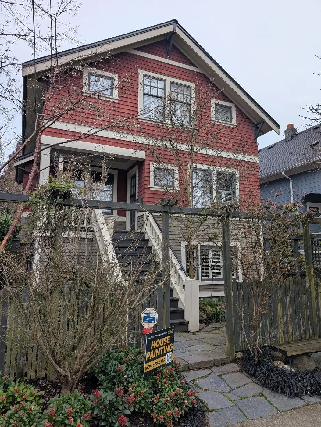 Weathered red craftsman house exterior in Vancouver, BC before repainting by Renaissance Painting, with peeling trim and faded siding visible from the front yard.