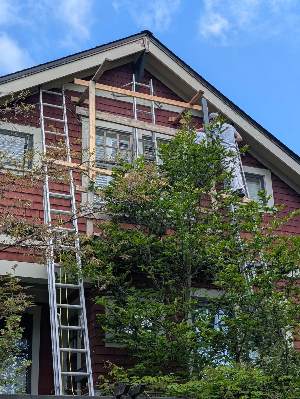 Renaissance Painting carpenter working from a ladder at the gable peak of a Vancouver, BC craftsman home, repairing trim before painting.