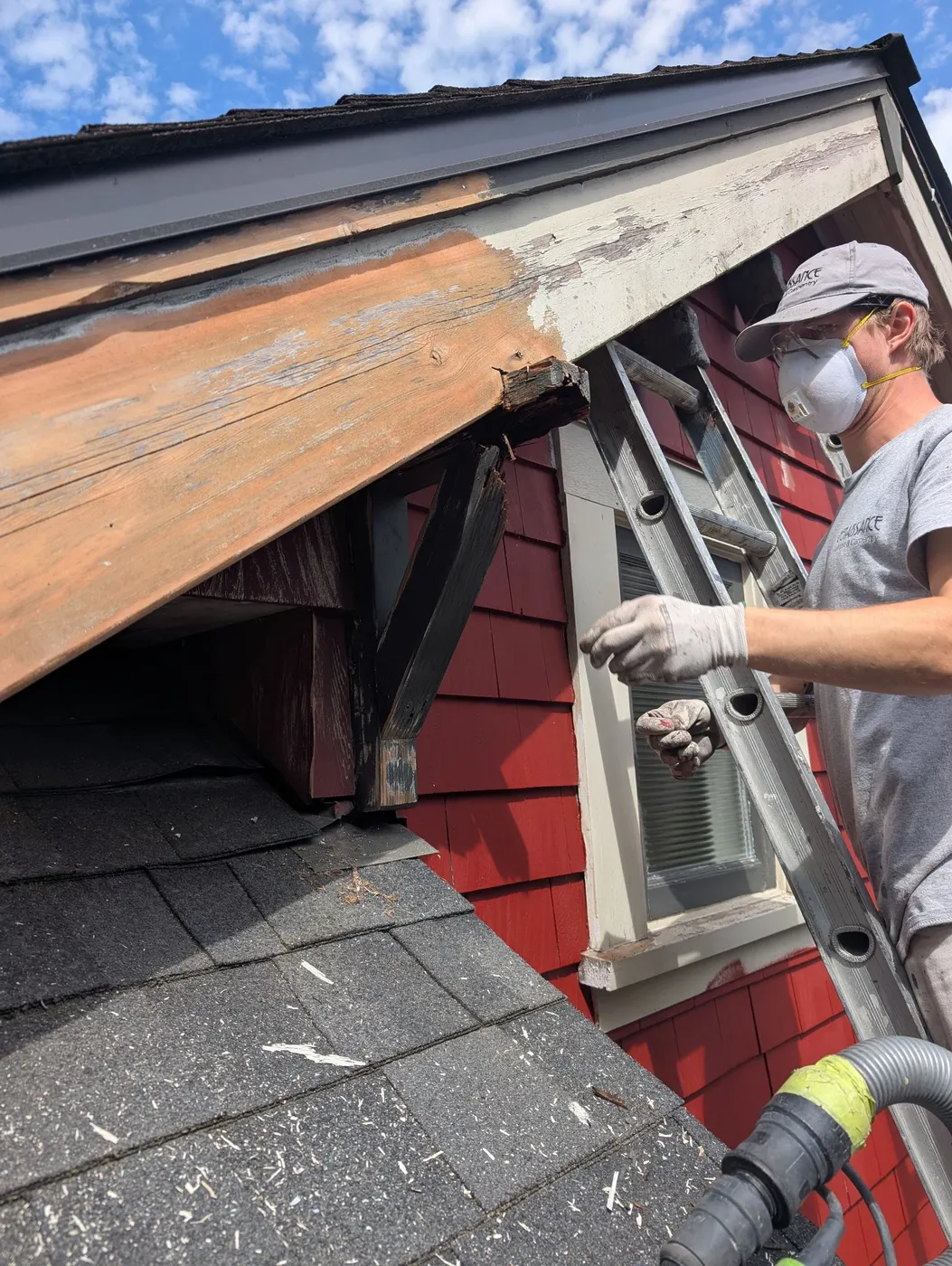 Renaissance Painting carpenter repairing rotted wood at the roof eave and fascia of a Vancouver, BC home, wearing safety glasses and a respirator.