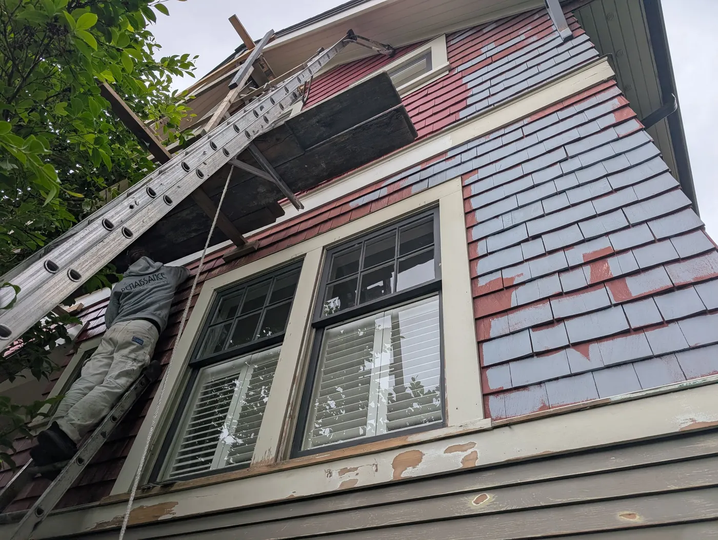 Renaissance Painting crew member on a ladder applying primer to cedar shingle siding over the original red paint on a Vancouver craftsman home.
