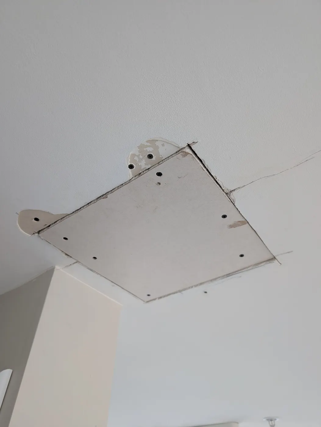 New drywall patch panel screwed into ceiling framing during an interior repair in a Vancouver, BC high-rise unit.