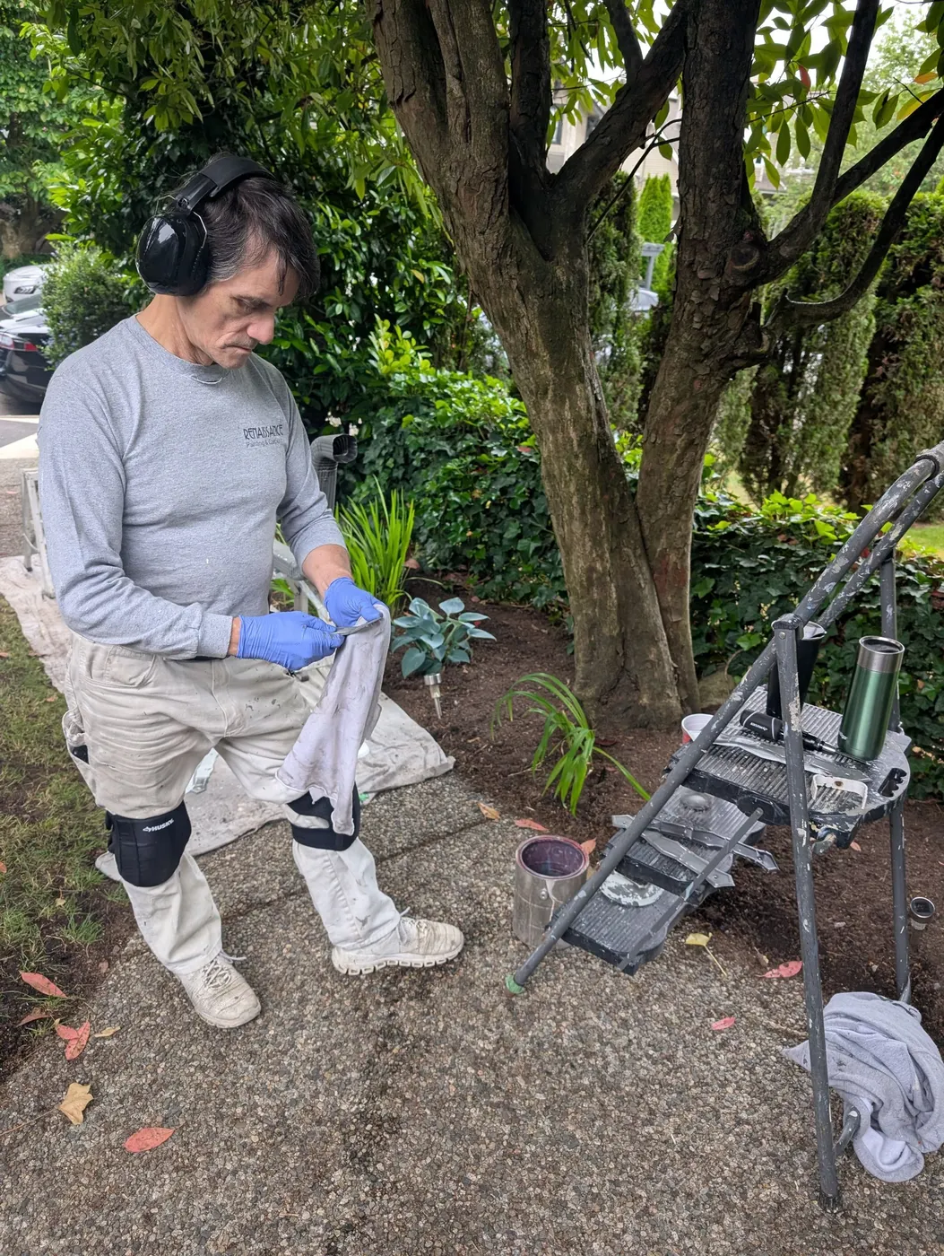 Renaissance Painting crew member cleaning brushes and tools beside a ladder and paint cans during an exterior repaint in Vancouver, BC.