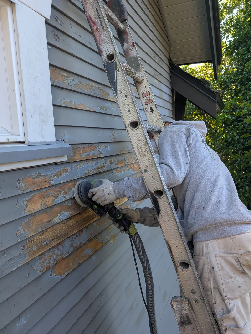 Painter sanding old peeling siding on a Vancouver, BC duplex before repainting