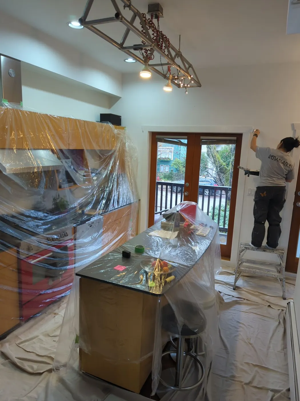 Painter on a ladder painting trim near a kitchen doorway during a Vancouver renovation.