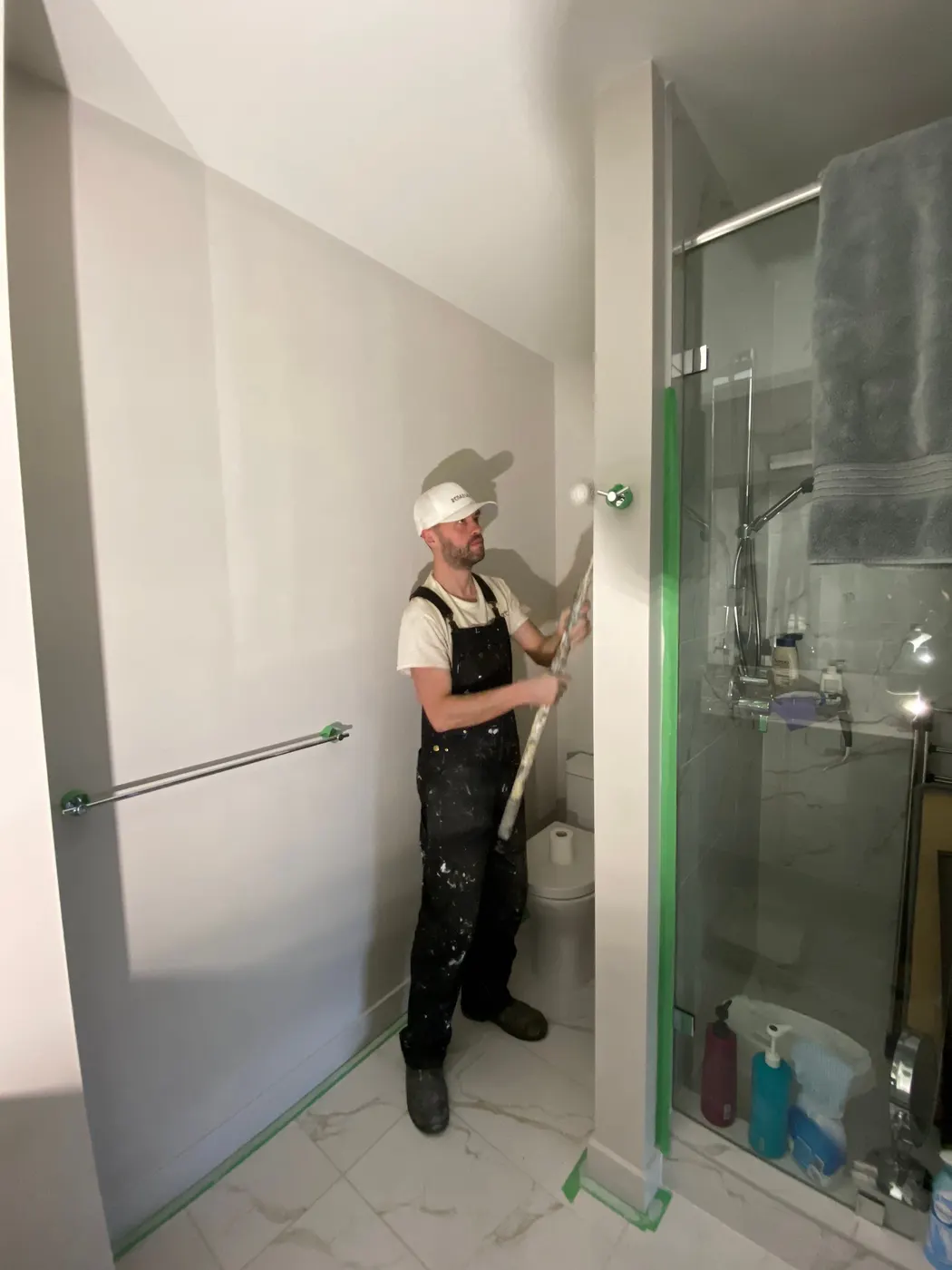 A painter cuts in fresh wall paint near a glass shower enclosure in a Vancouver, BC bathroom renovation.