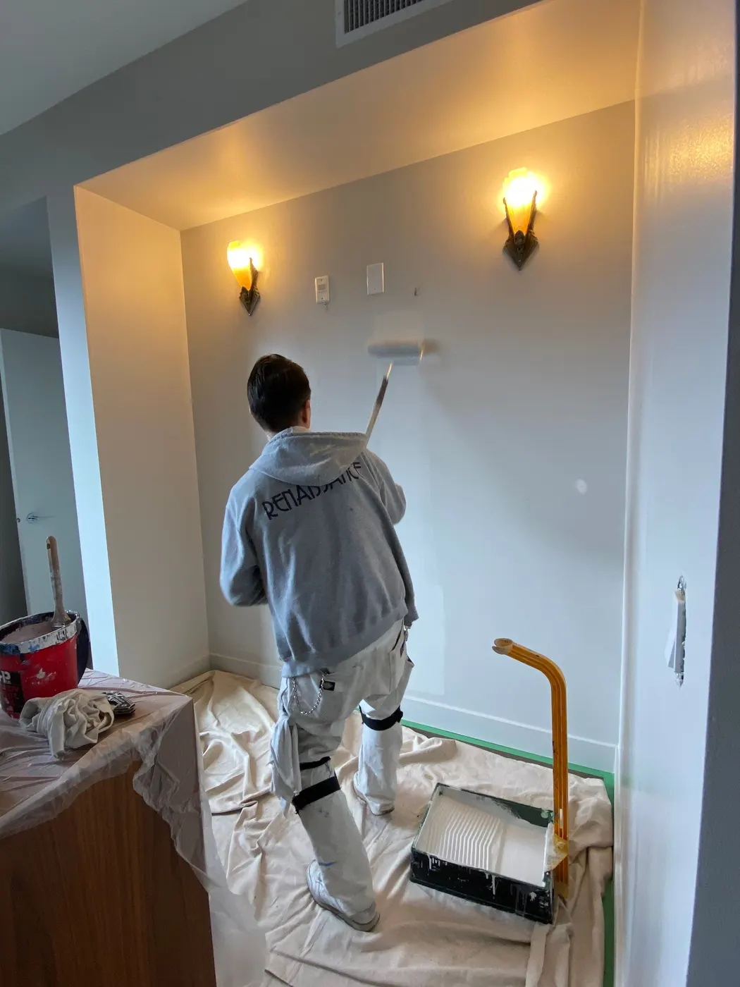 A painter rolls a fresh coat of paint on a wall between two vintage sconces in a Vancouver, BC apartment.