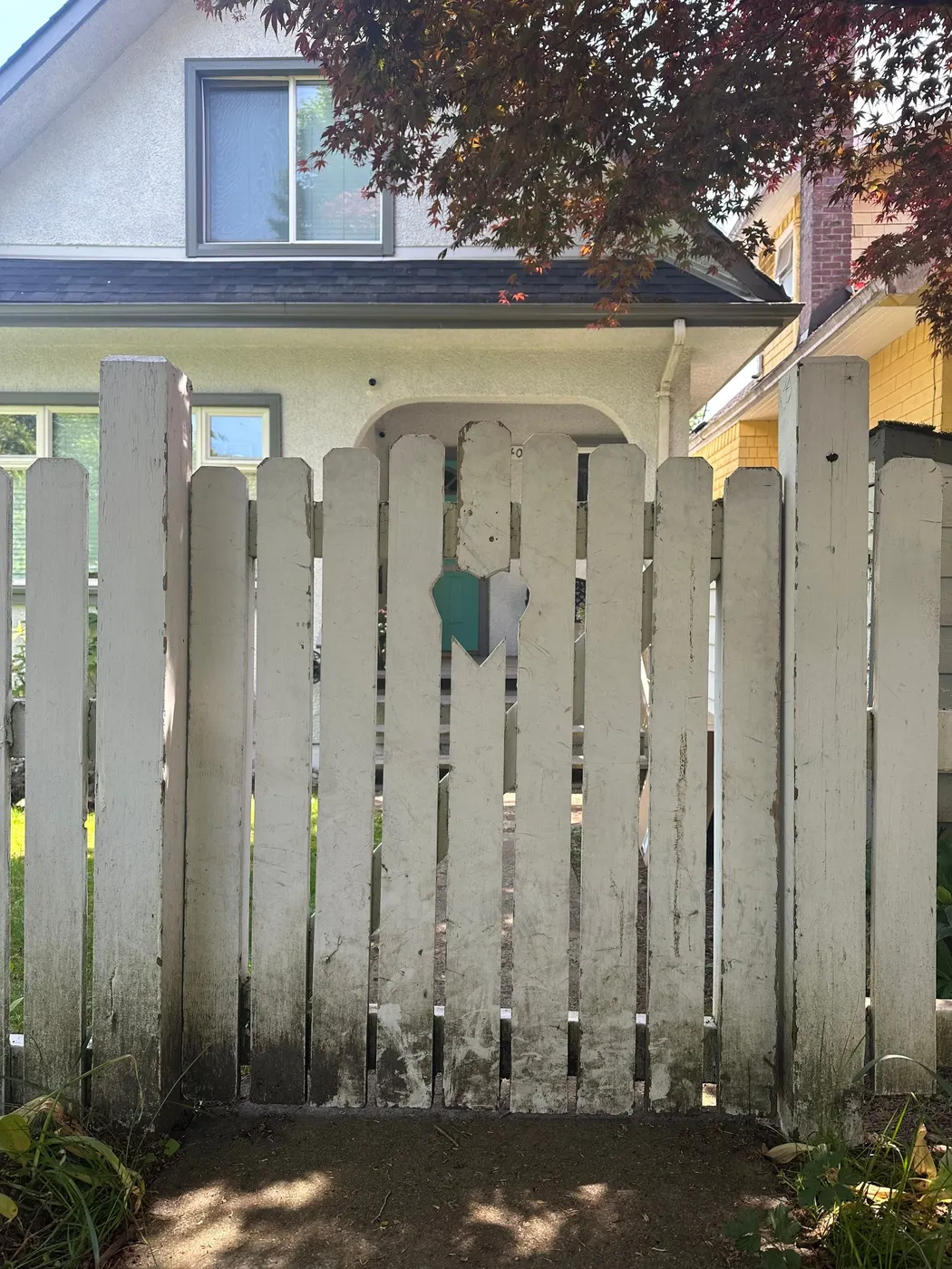 Weathered white picket fence gate with peeling paint before restoration in Vancouver, BC