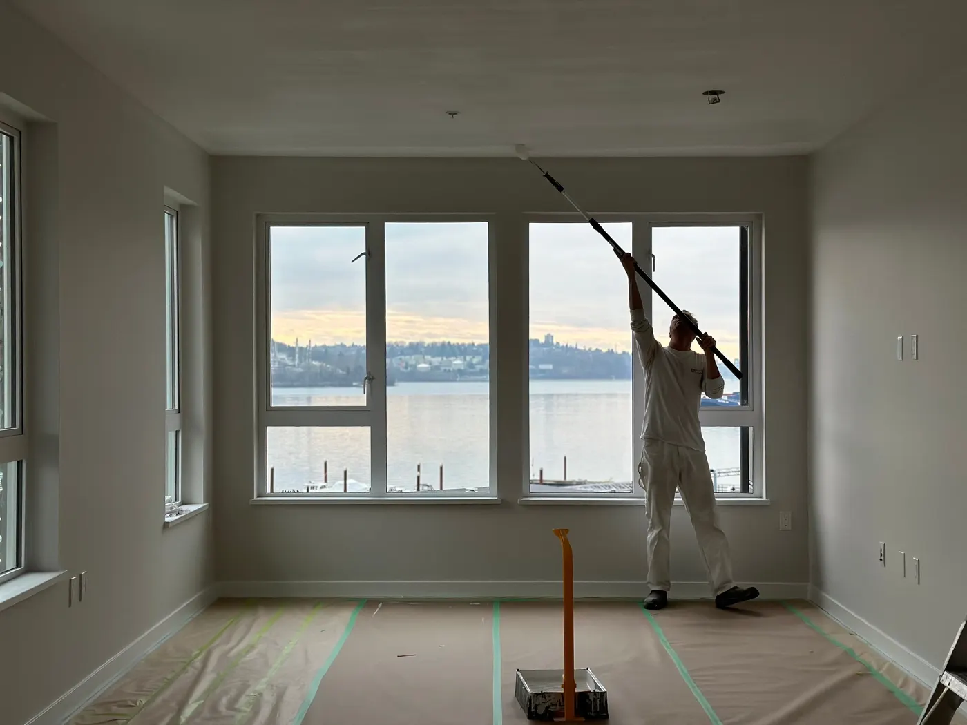 Painter using an extension pole to roll ceiling paint in a Vancouver, BC condo with a waterfront view, part of an interior repaint by Renaissance Painting.