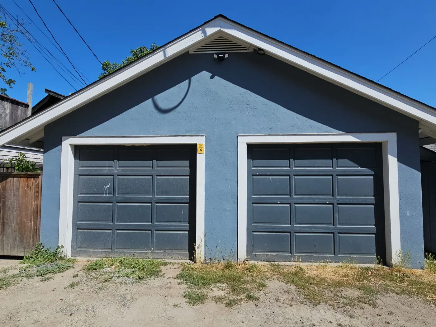 Weathered blue stucco garage with peeling paint on the gable trim before exterior painting in Vancouver, BC