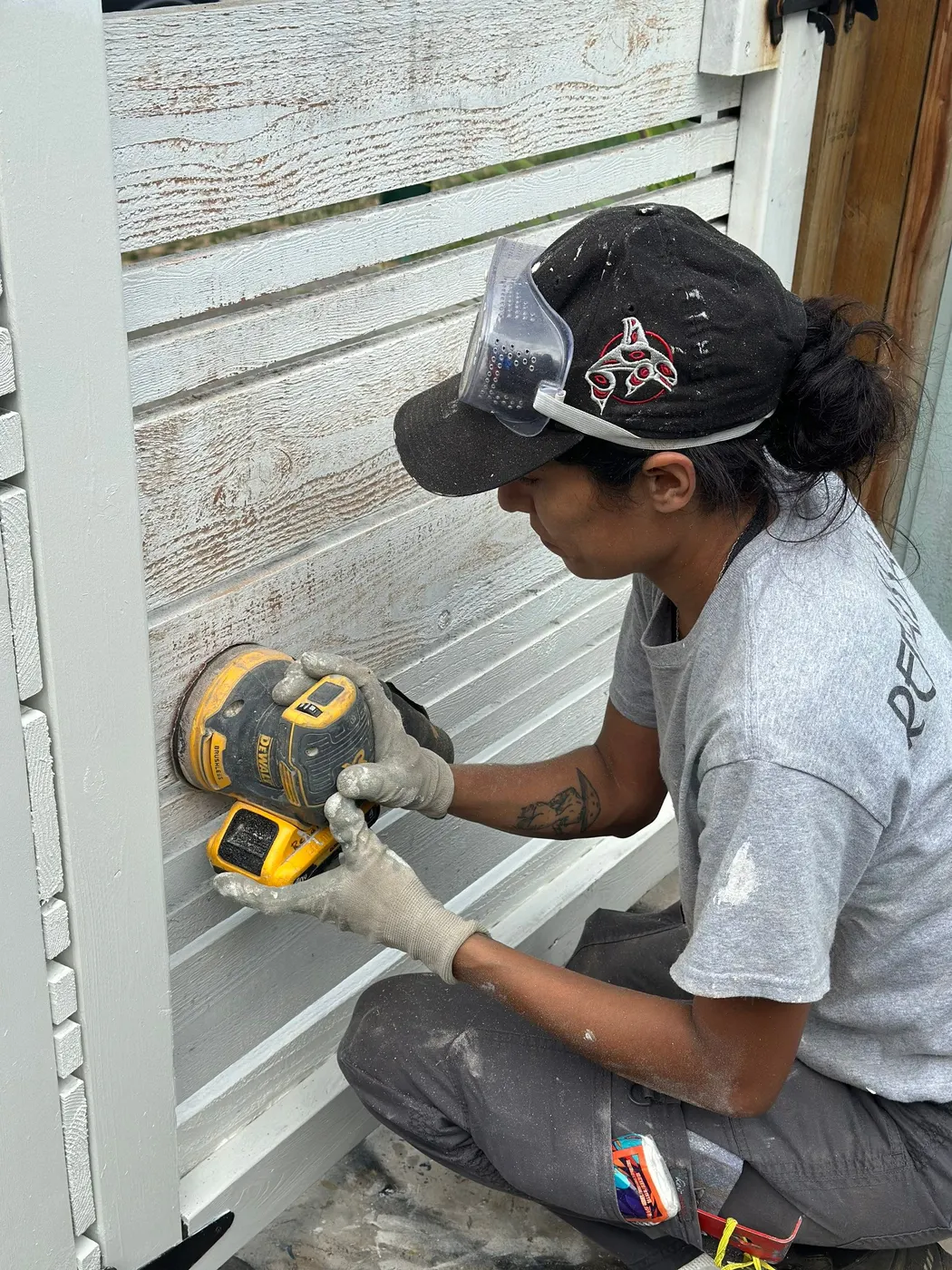 Renaissance Painting crew member sanding white-painted wood siding with a dust-extraction orbital sander on a Vancouver, BC home exterior.