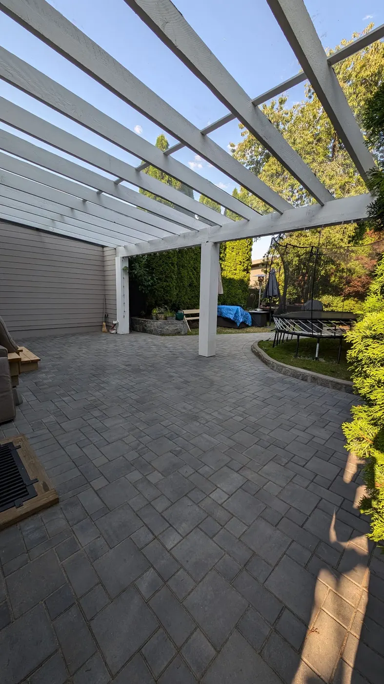 White painted wood pergola over a stone patio in a Vancouver, BC backyard