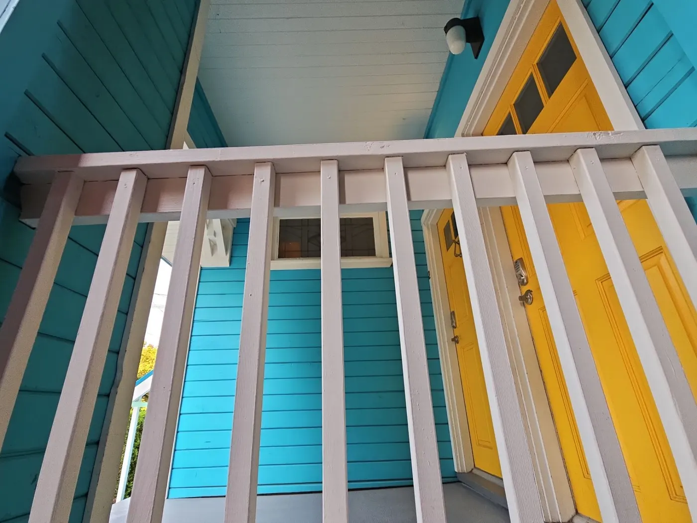 Upward view of a newly painted porch ceiling, white railing, and yellow entry doors on a Vancouver home by Renaissance Painting.