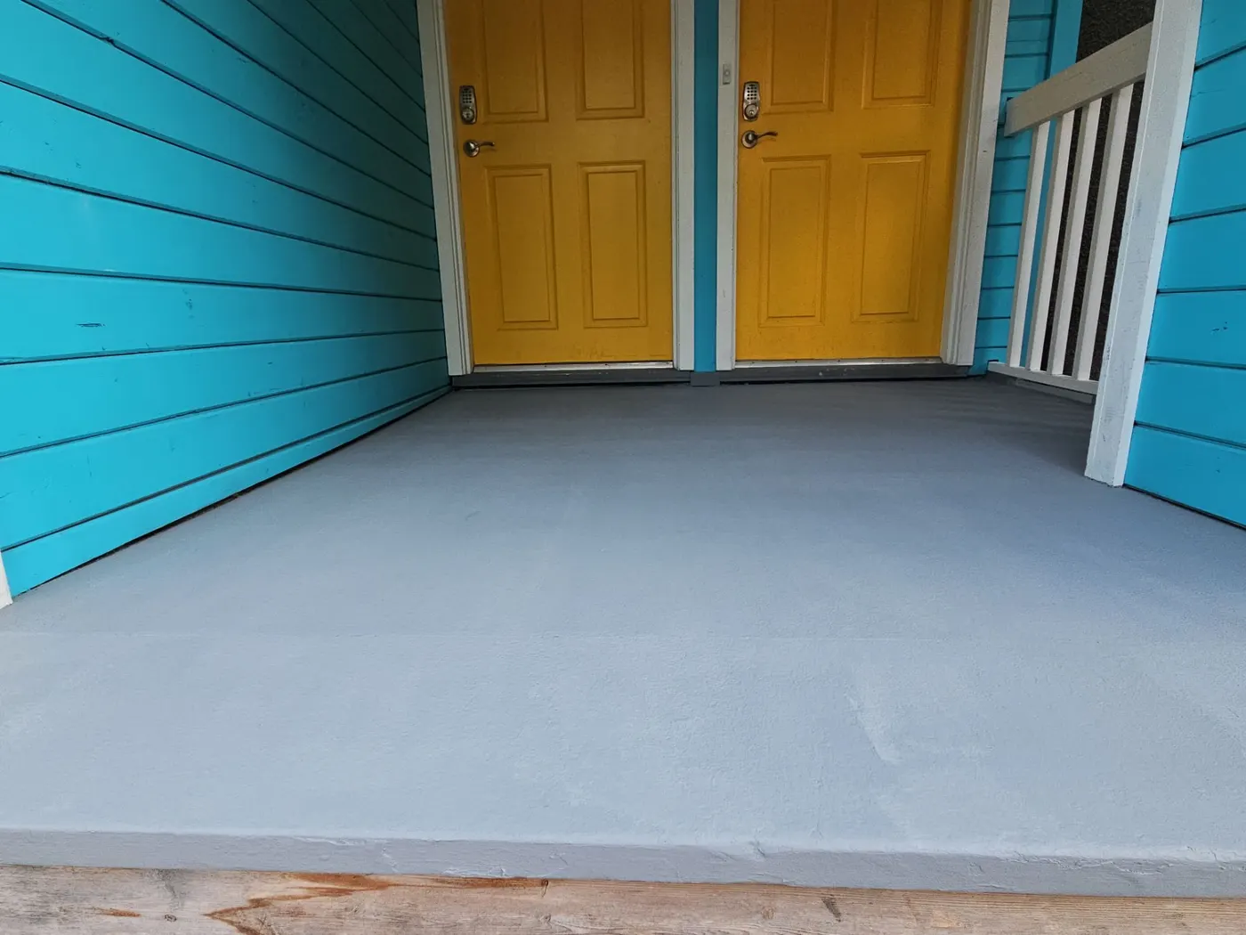 Freshly painted grey porch deck floor between two yellow doors on a Vancouver, BC front porch.