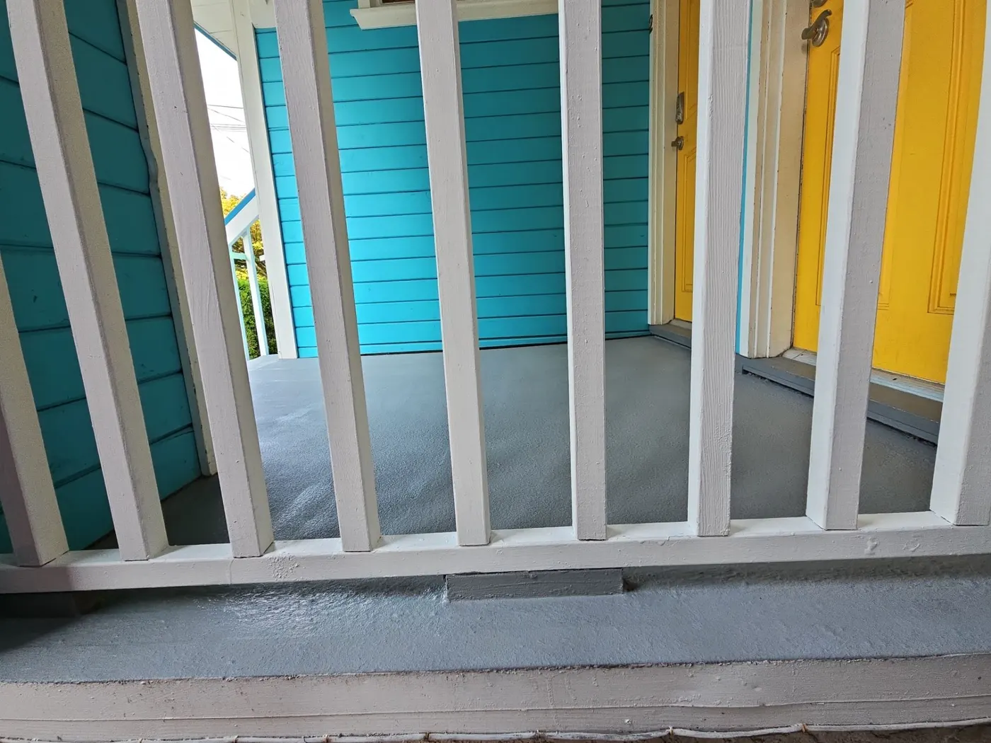 Freshly painted turquoise front porch with white railing and yellow front doors on a Vancouver, BC duplex, completed by Renaissance Painting.