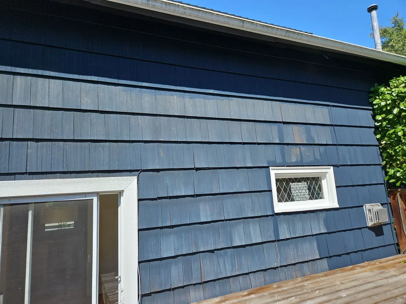 Before and after color contrast on blue shingle siding beside a leaded glass window in Vancouver, BC.
