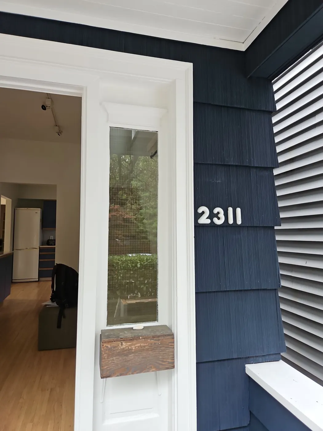 House number and painted white window trim against navy blue shingle siding in Vancouver, BC.