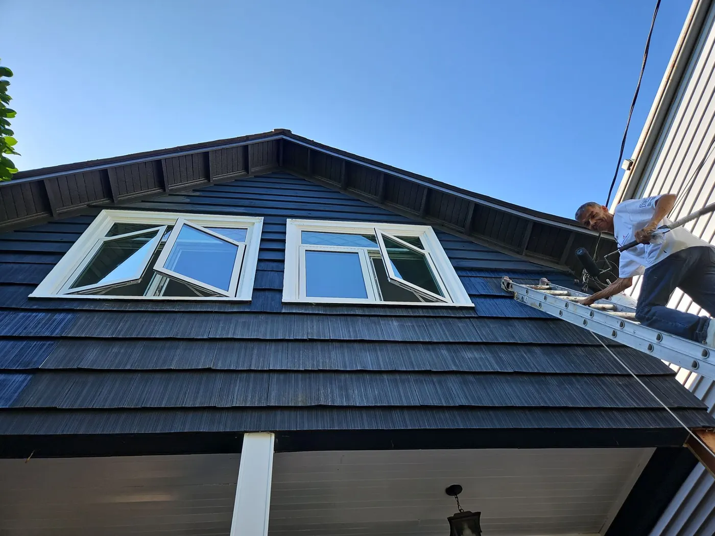 Painter on an extension ladder working near dormer windows on a Vancouver, BC home exterior.