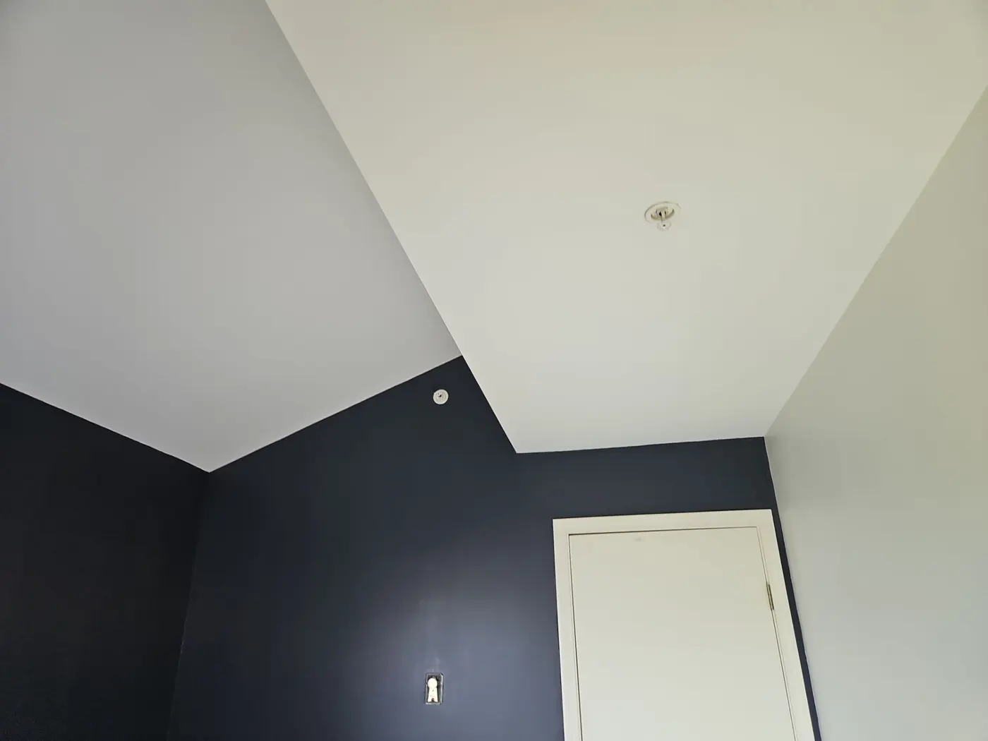 Freshly painted navy wall meeting a white vaulted ceiling with a fire sprinkler head in a Vancouver, BC bedroom.