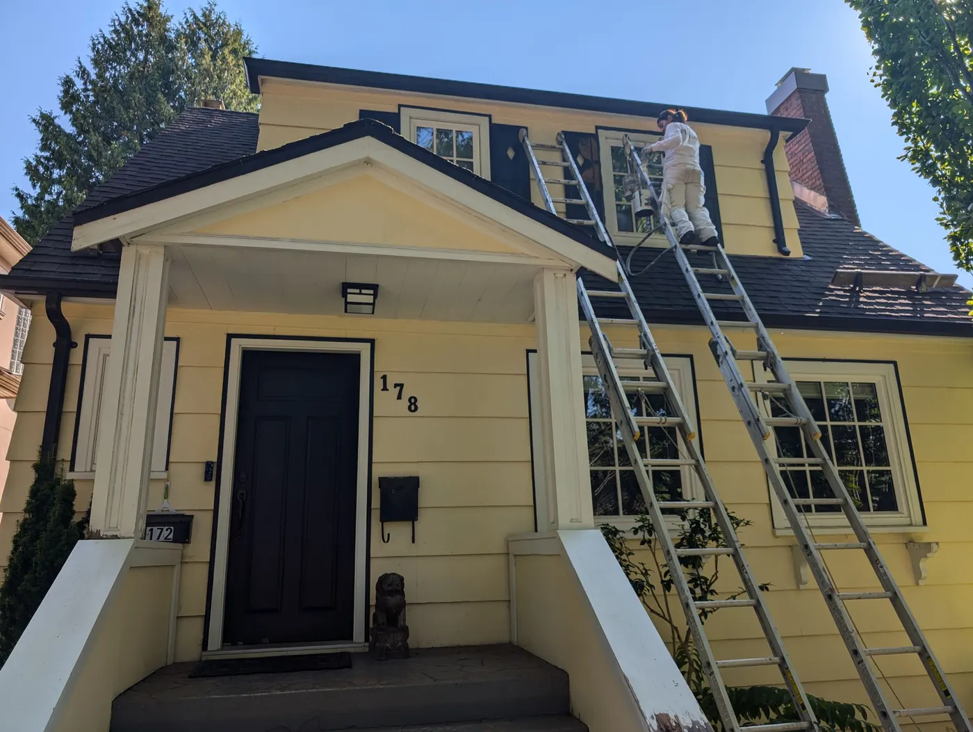 Painter on extension ladder repainting the upper dormer trim of a Vancouver character home during an exterior painting project by Renaissance Painting.