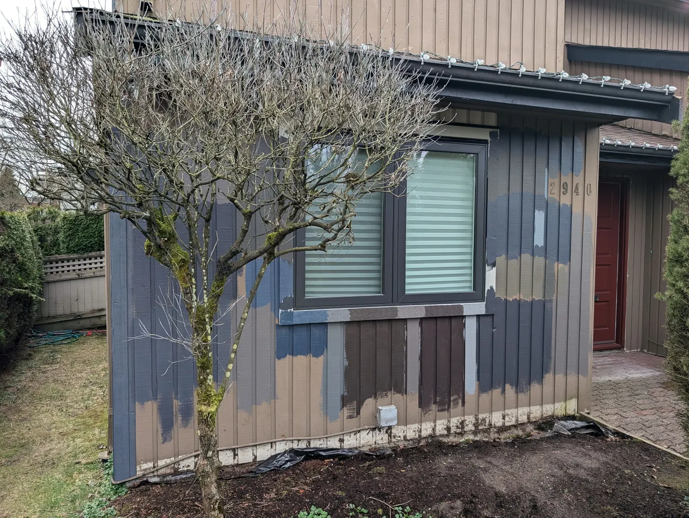 Corner of a Vancouver townhome showing several exterior paint color test patches on wood siding near a window.