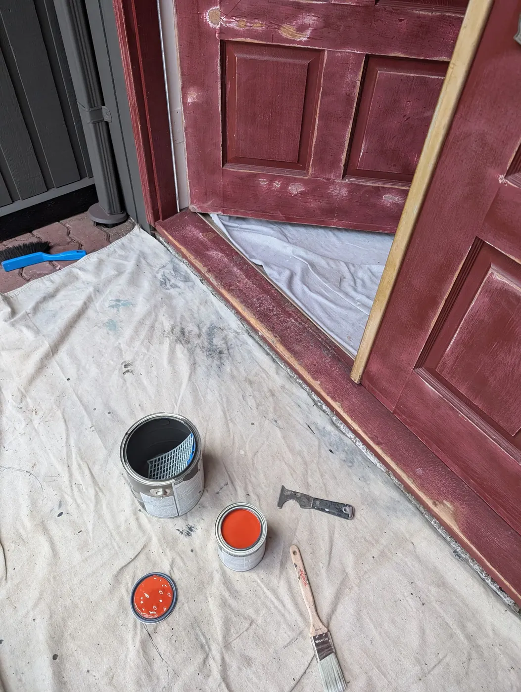 Maroon front door being refinished with fresh paint cans and brushes on the porch of a Vancouver home.